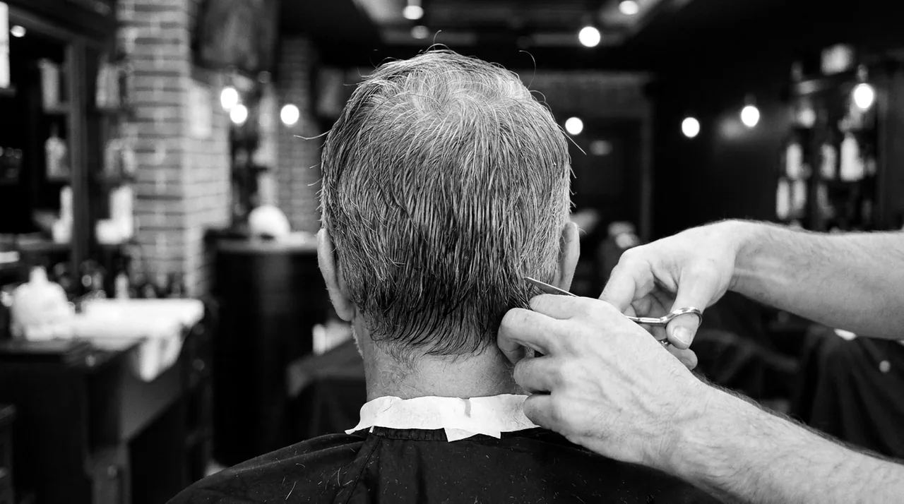 Cheveux gris humides, vus de dos : le barbier tient une mèche à la nuque et coupe aux ciseaux