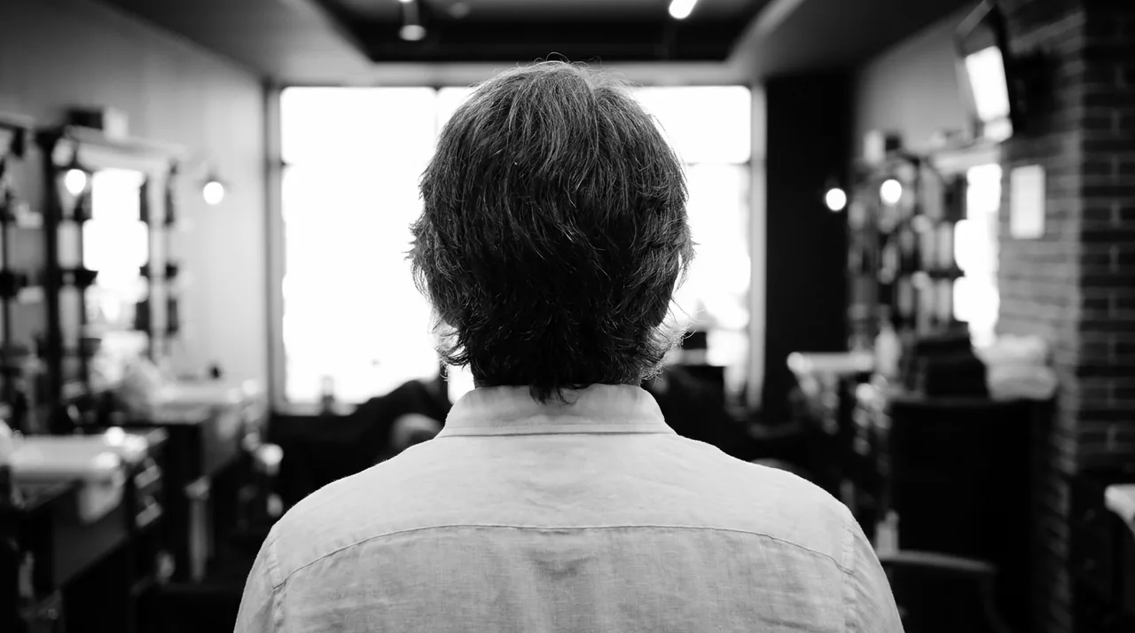Homme aux cheveux grisonnants couvrant les oreilles, vu de dos face à une vitrine lumineuse