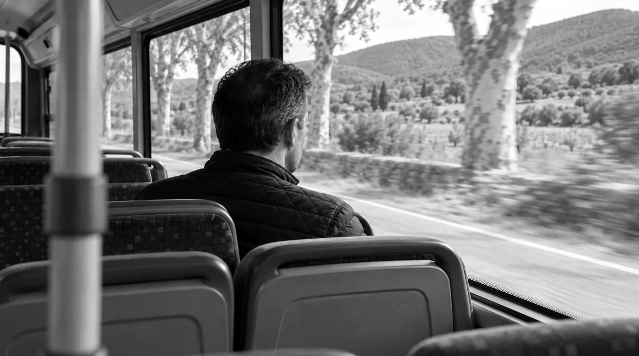 Homme vu de dos assis dans un bus régional presque vide, regardant par la fenêtre une route de campagne