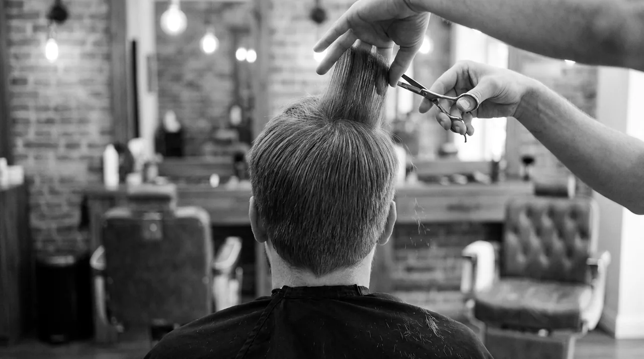 Mains d'un barbier coupant aux ciseaux une mèche pincée sur le dessus du crâne